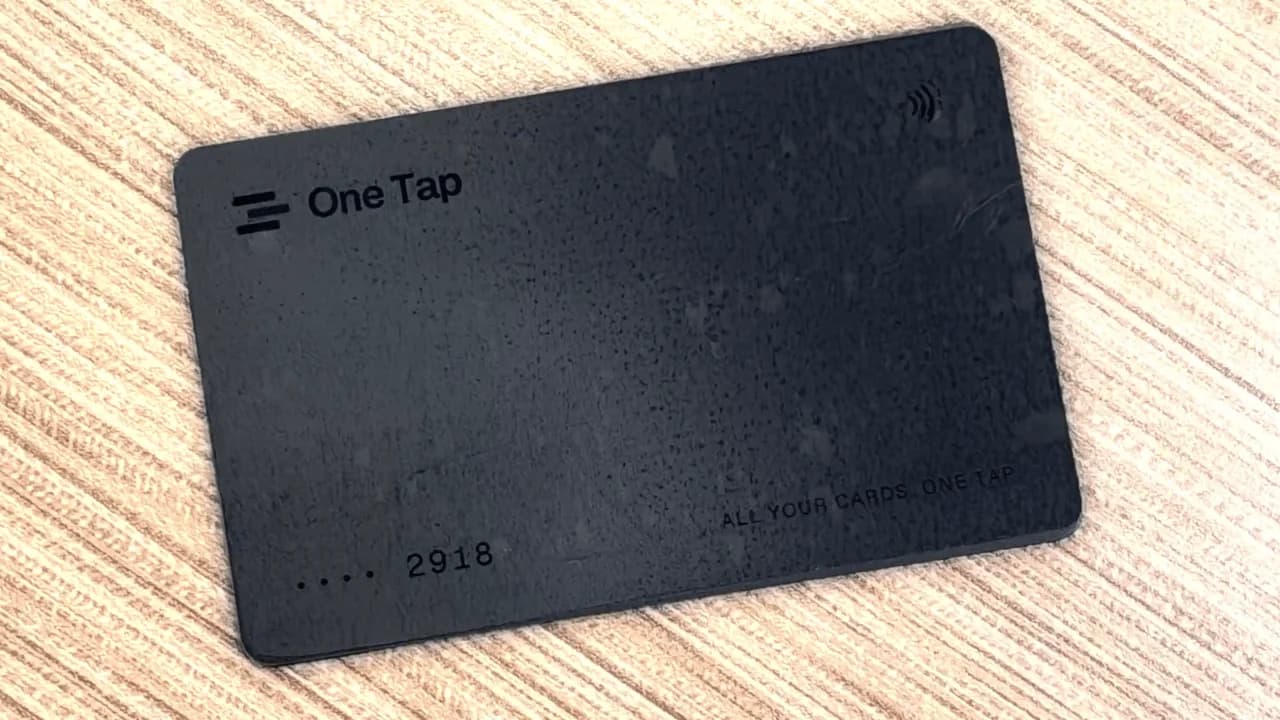 A matte black OneTap card reading “All your cards. One tap” on a wooden desk
