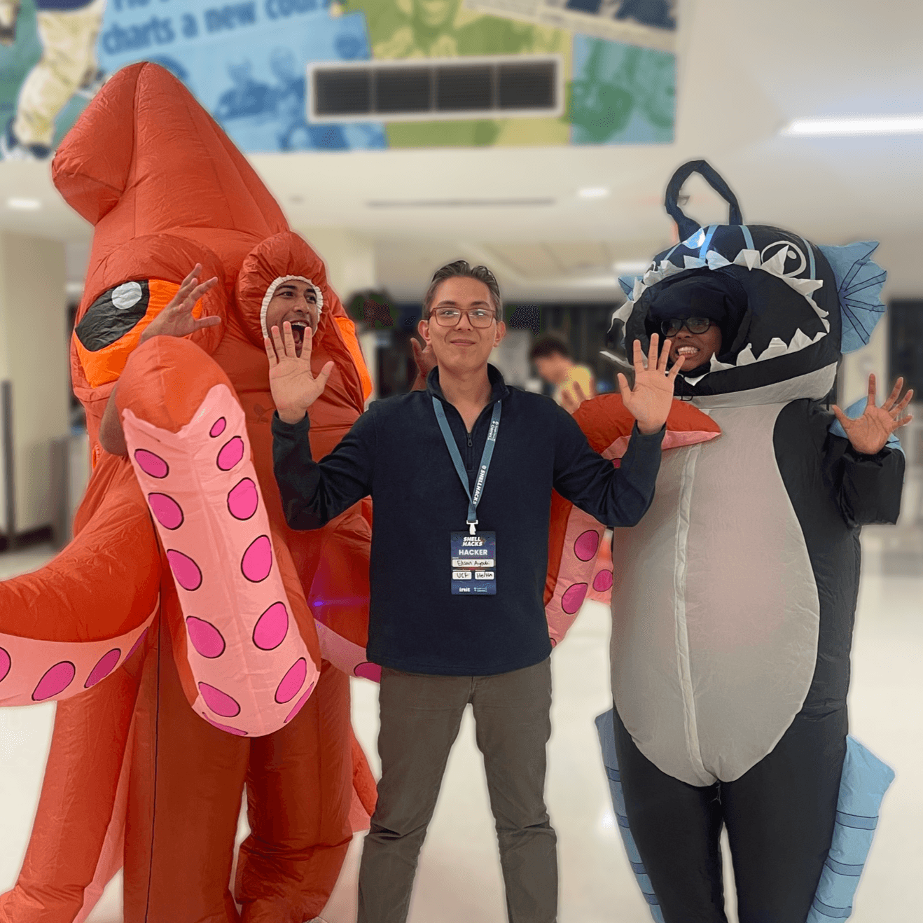 Ehsan at ShellHacks with hands up, between friends in inflatable squid and anglerfish costumes